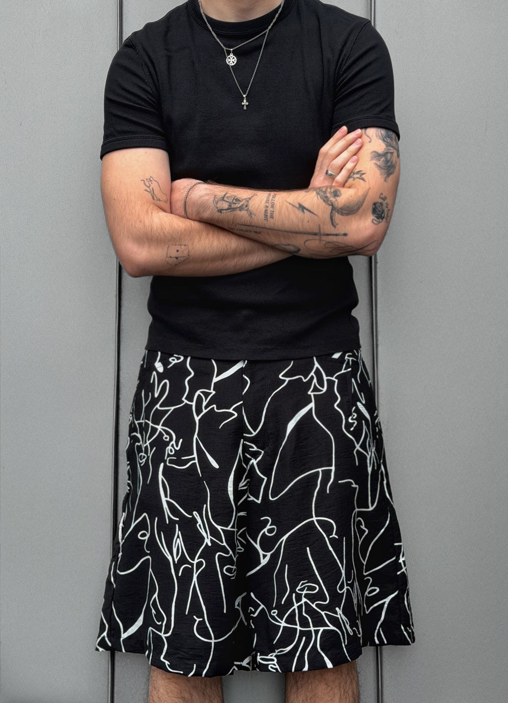 Person wearing a black t-shirt and black shorts with white abstract patterns against a gray background