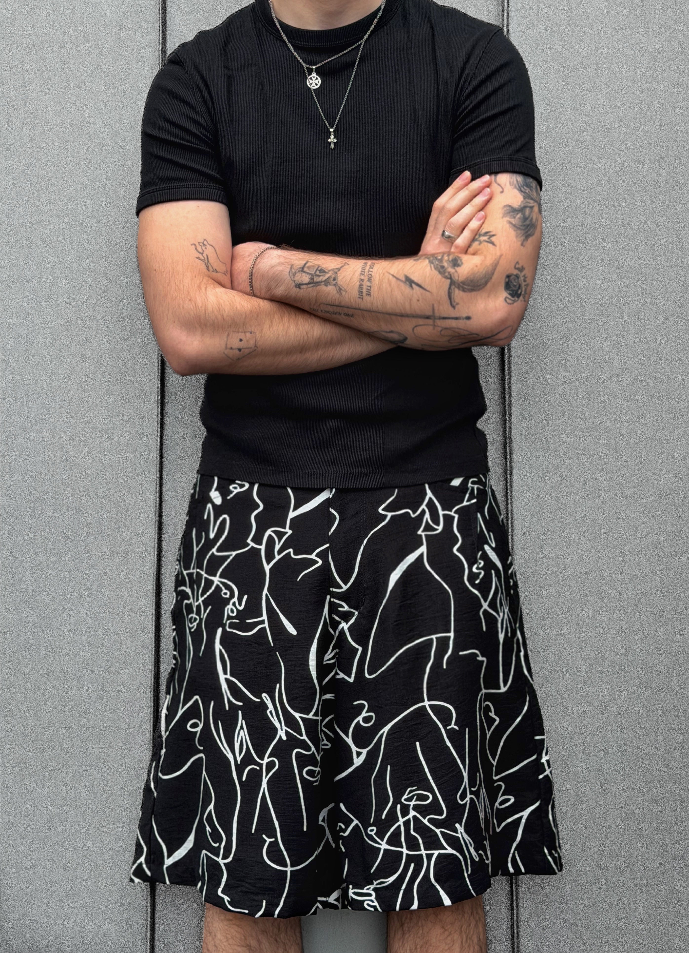 Person wearing a black t-shirt and black shorts with white abstract patterns against a gray background