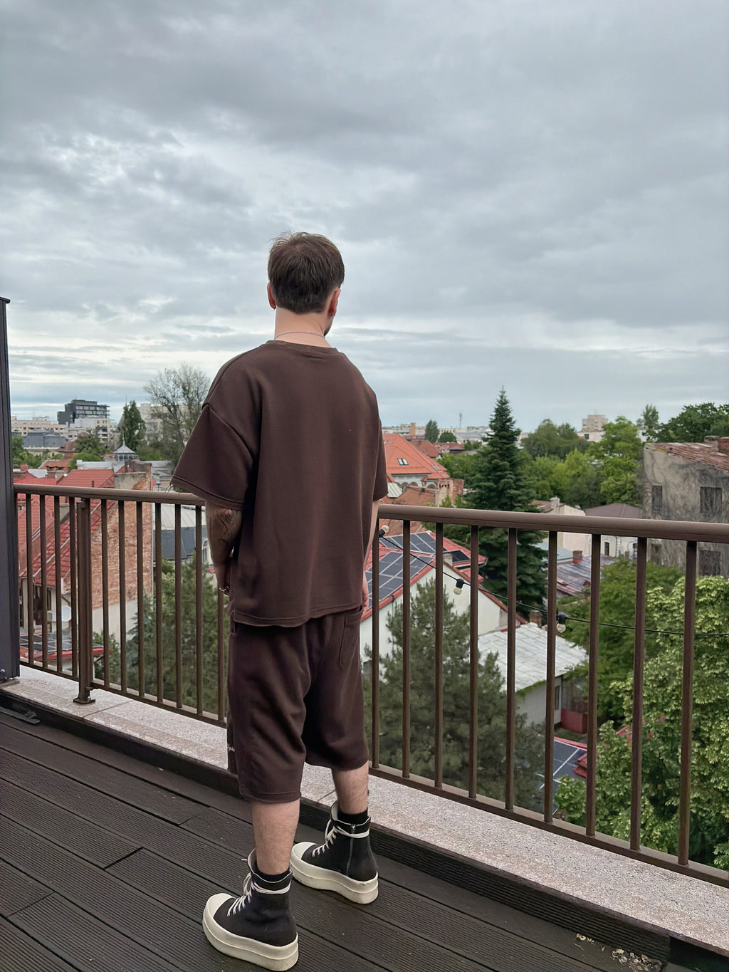 Person standing on a balcony overlooking a cityscape with a cloudy sky.