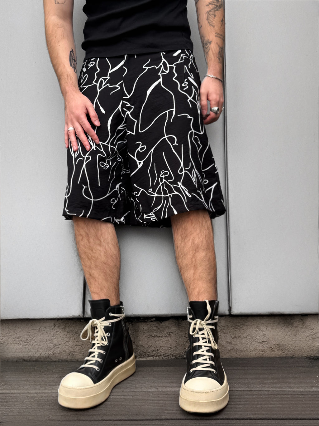 Person wearing a black and white patterned skirt with high-top sneakers against a plain background