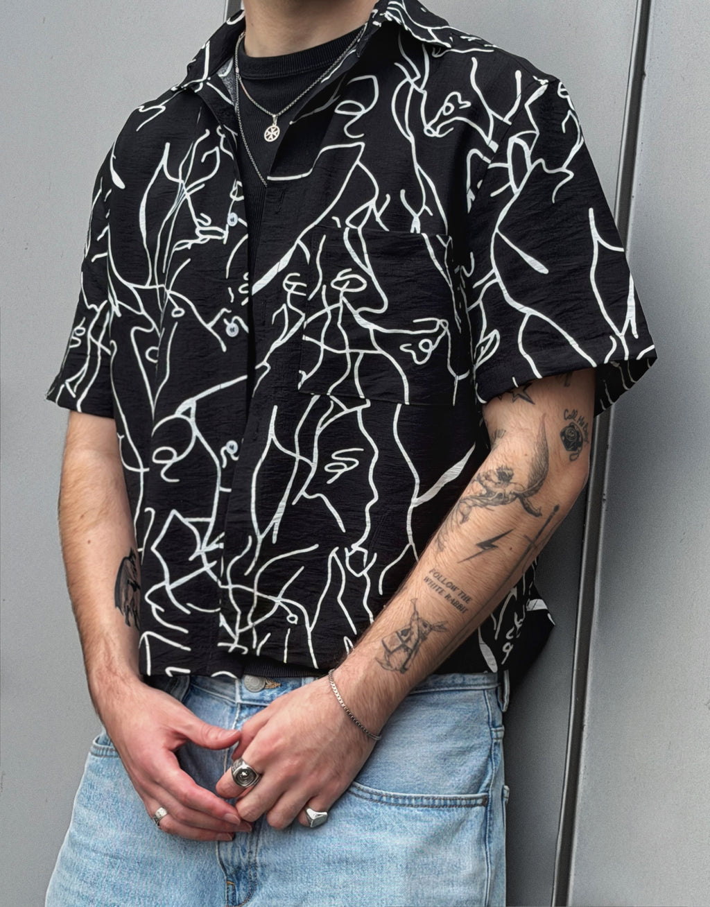 Person wearing a black shirt with white abstract patterns and light blue jeans against a gray background