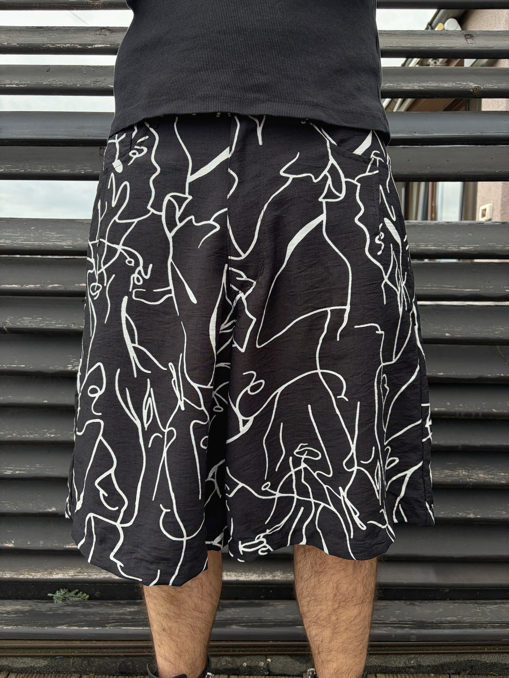 Person wearing black shorts with white abstract patterns against a metallic background