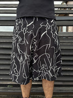 Person wearing black shorts with white abstract patterns against a metallic background
