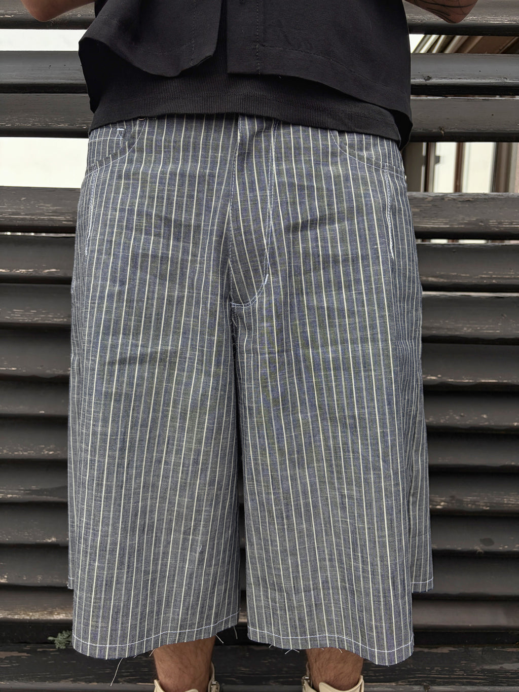 Person wearing gray checkered shorts with a black top against a metallic background