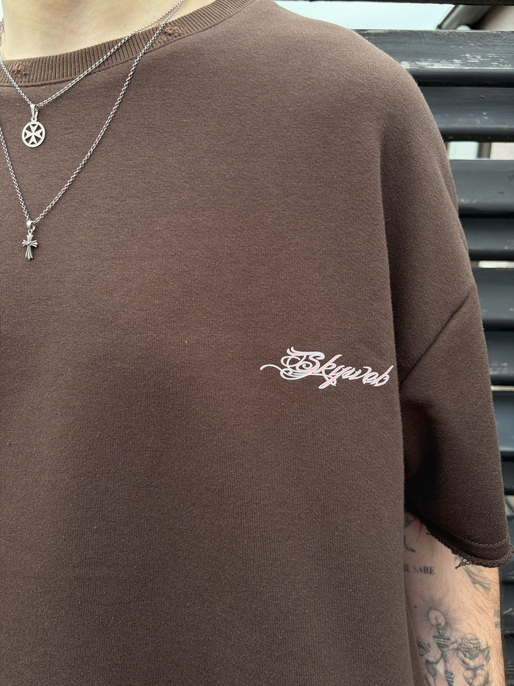Brown sweatshirt with 'Skywear' logo on a person wearing necklaces.