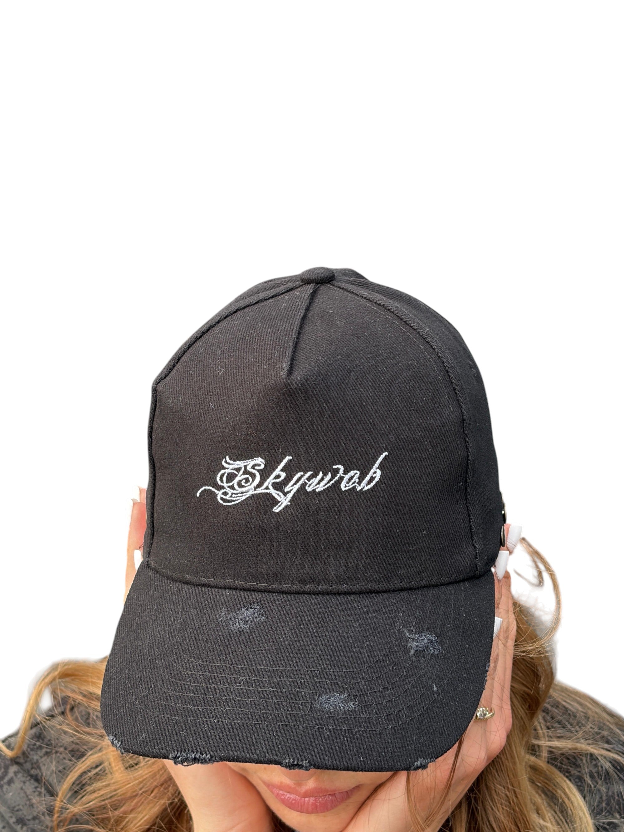 Black distressed cap with 'Skyweb' logo worn by a person on a white background