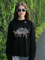 A woman wearing a black crewneck sweatshirt with a distressed hole in the chest and a graphic of two cheetahs walking in front of mountains, standing outdoors against a green ivy-covered wall.