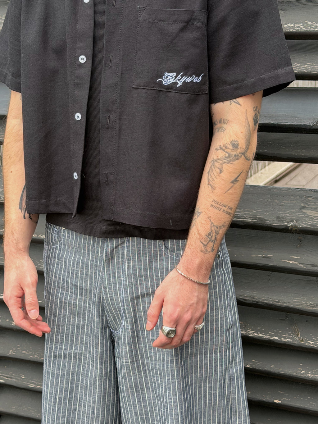 Person wearing a black shirt with a logo and plaid pants standing on metal stairs.