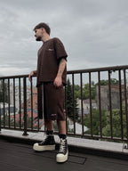 Man wearing a brown outfit standing on a balcony with a cityscape background