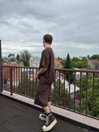 Person standing on a balcony overlooking a cityscape with green trees and rooftops.
