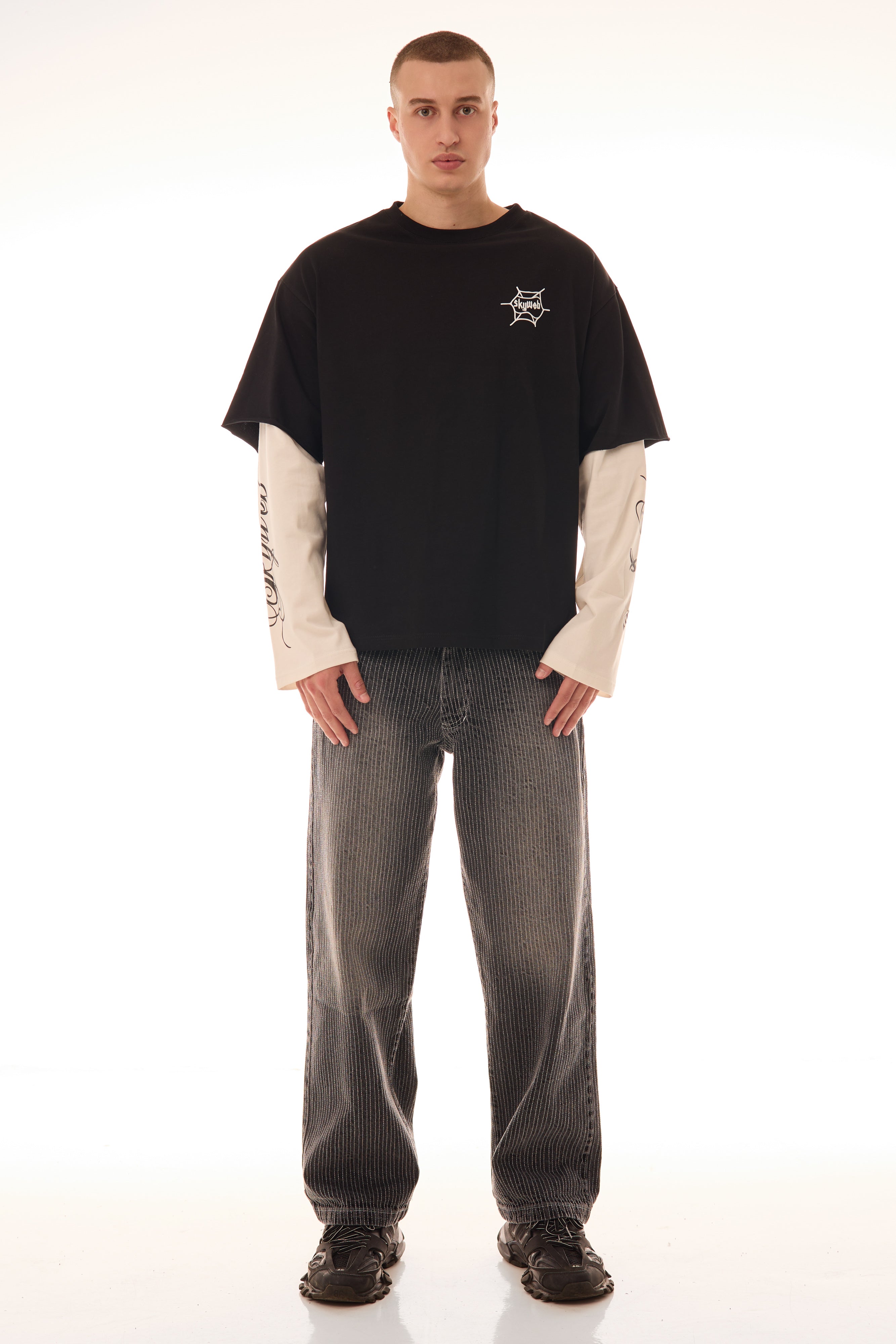 Model purtând tricoul DUAL LONG TEE Skyweb, tricou negru cu mâneci albe layered și print pe piept – vedere frontală.