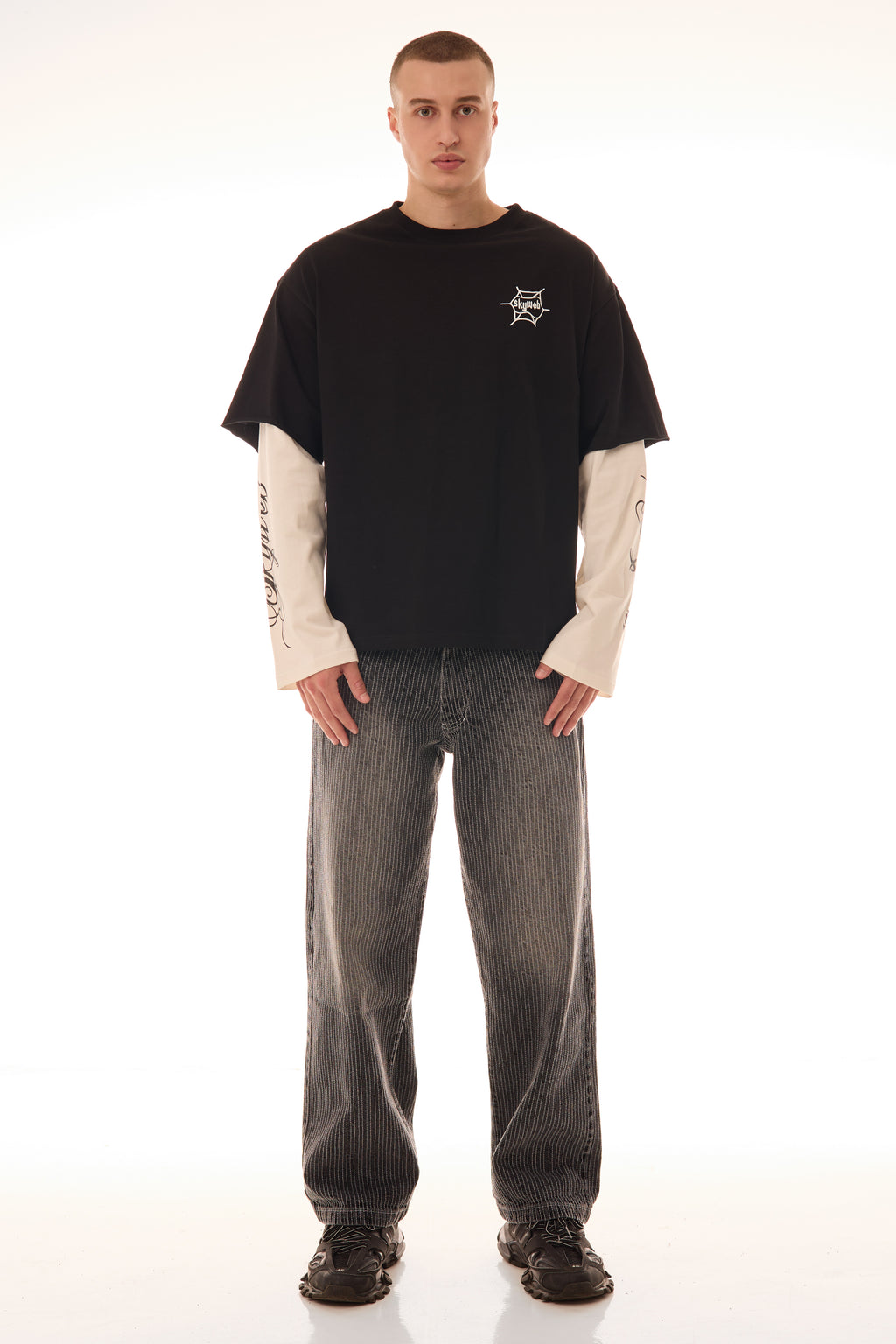 Model purtând tricoul DUAL LONG TEE Skyweb, tricou negru cu mâneci albe layered și print pe piept – vedere frontală.