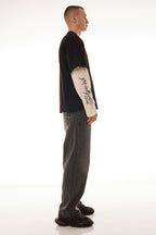 Model văzut din lateral purtând tricoul DUAL LONG TEE Skyweb, tricou negru cu mâneci albe layered și print gotic pe mâneci.