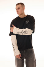 Model în poziție 3/4 purtând tricoul DUAL LONG TEE Skyweb, tricou negru cu mâneci albe layered și print gotic pe mâneci.