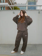 SKYWEB model wearing a dark brown matching hoodie and wide-leg sweatpants set with white sneakers in an urban setting.