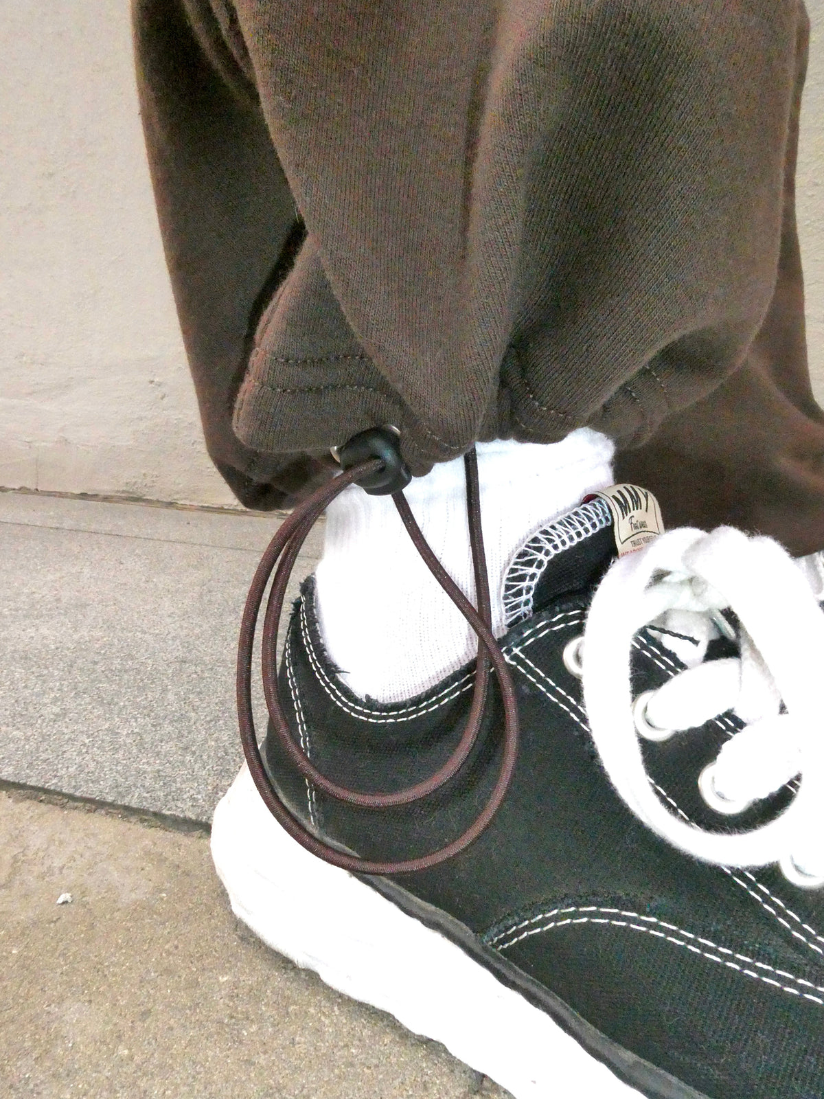SKYWEB rust sweatpants featuring an adjustable hem with a black cord stopper cinched over a black and white sneaker