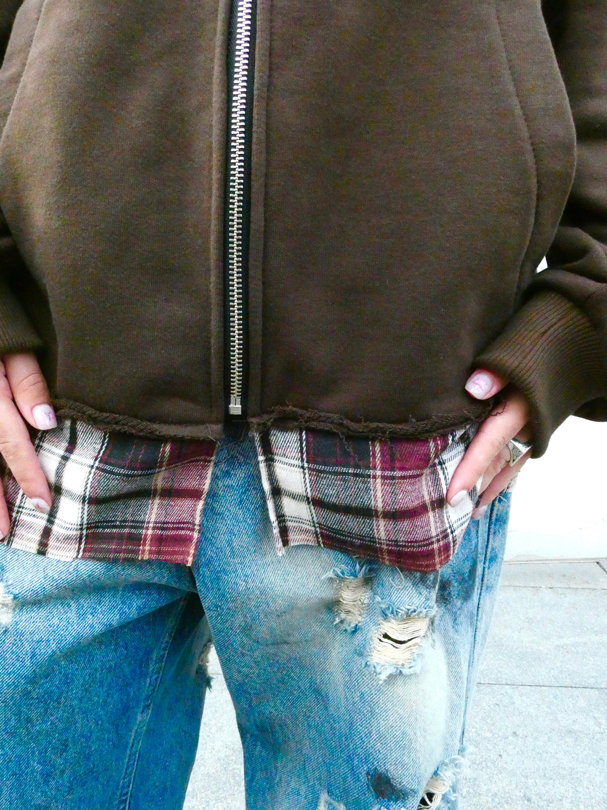 SKYWEB rust zip-up hoodie featuring a raw exposed seam and extended patchwork plaid flannel hem over distressed jeans.